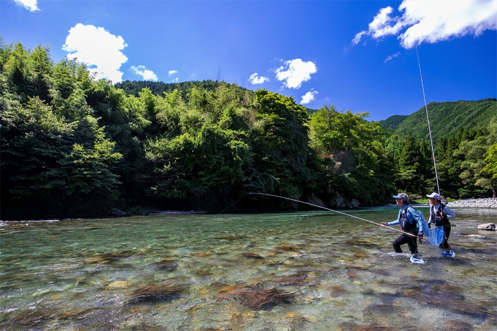 「ここまで青く澄んだ流れを釣るのは初めて」と話す湯川さんに「明るく見える石をねらってください」とアドバイスする島さん